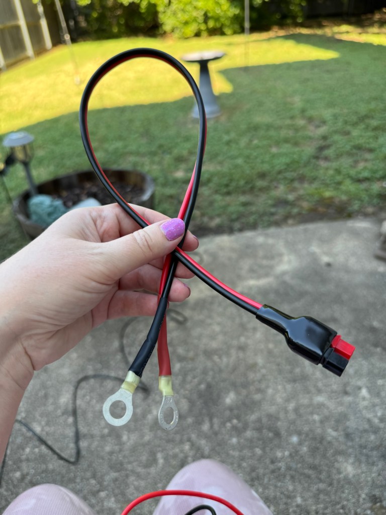 A photograph of a cord in my hand. One end of the cable has two ring terminals and the other has a set of Anderson Powerpole connectors.